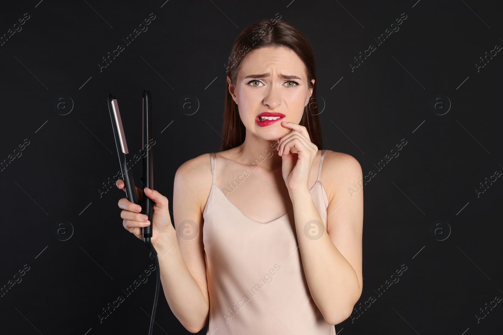 Photo of Upset young woman with flattening iron on black background. Hair damage