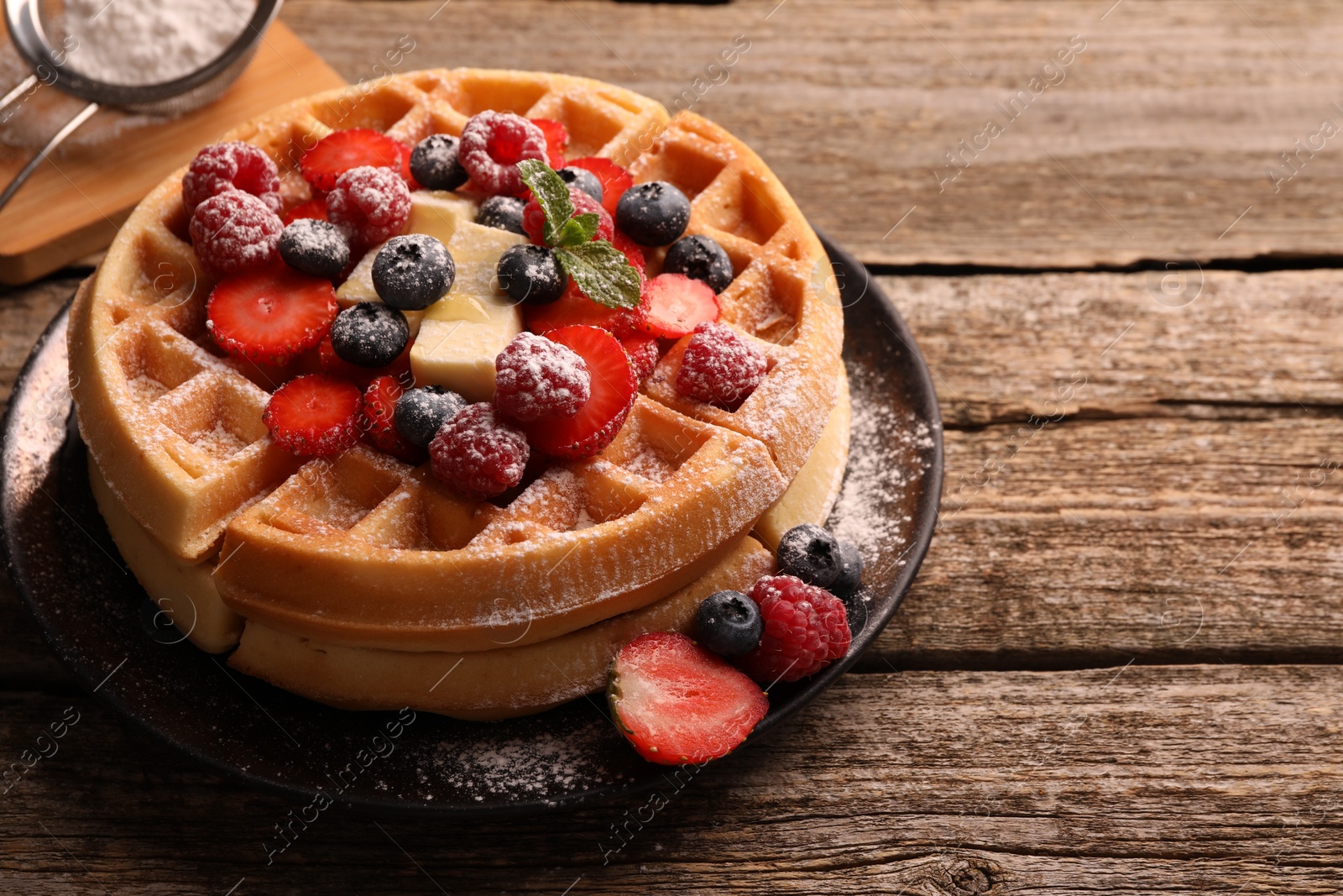 Photo of Tasty Belgian waffles with fresh berries, cheese and powdered sugar on wooden table, closeup. Space for text