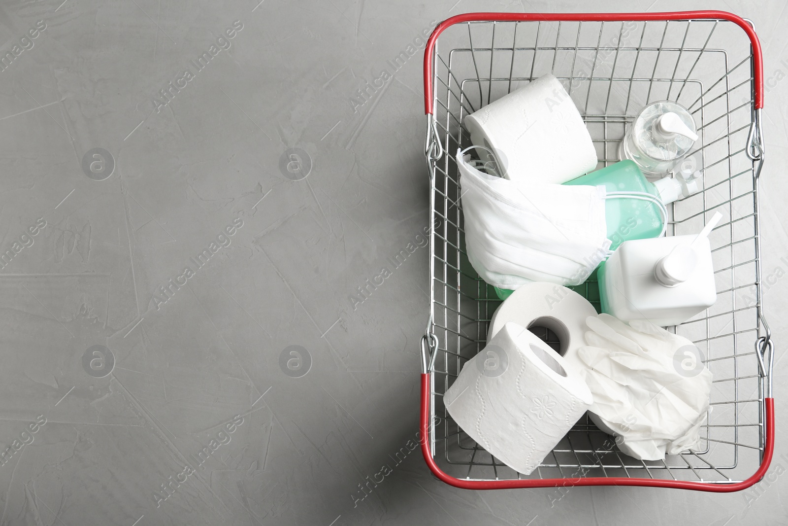 Photo of Top view of shopping basket with antiseptics, toilet paper, gloves and masks on light grey stone table, space for text. Panic caused by virus