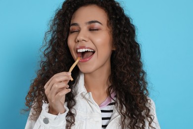 Photo of African American woman eating French fries on light blue background