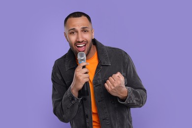 Photo of Handsome man with microphone singing on violet background