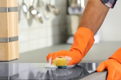 Man cleaning kitchen stove with sponge, closeup