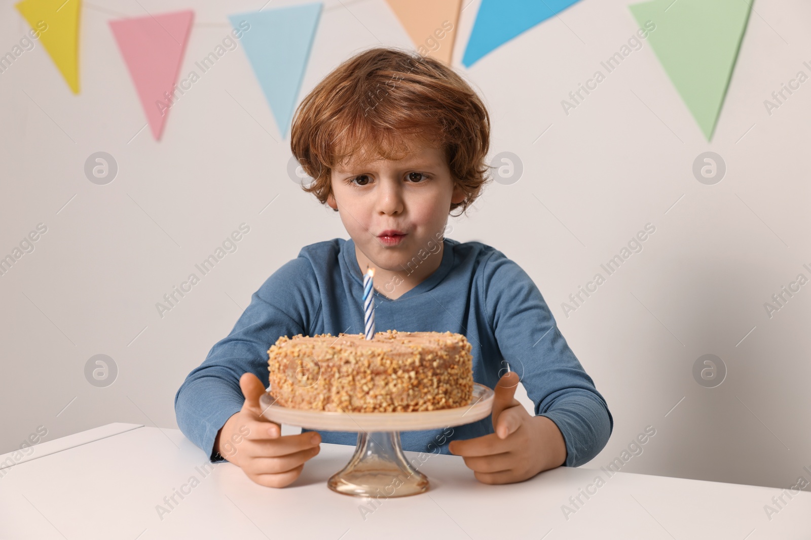 Photo of Cute boy with birthday cake at white table indoors