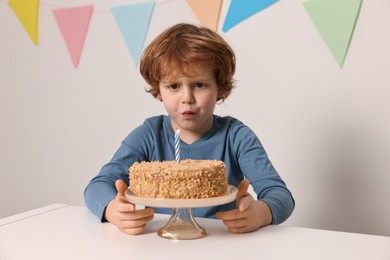 Cute boy with birthday cake at white table indoors