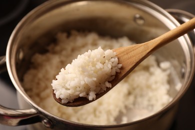 Wooden spoon with delicious rice over pot, closeup