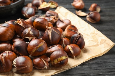 Photo of Tasty roasted edible chestnuts on black wooden table, closeup