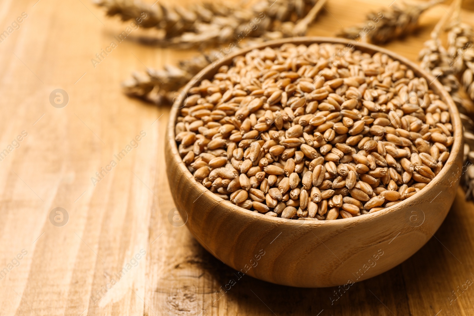 Photo of Wheat grains with spikelets on wooden table, closeup