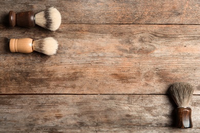 Photo of Flat lay composition with men's shaving brushes and space for text on wooden background