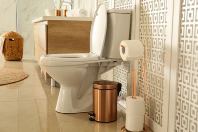 Photo of Toilet bowl near wooden screen in modern bathroom interior