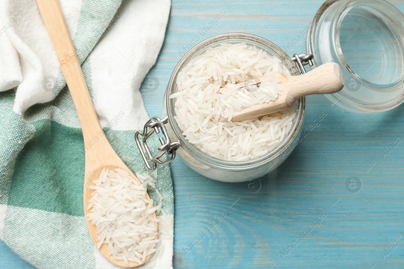 Photo of Raw basmati rice in jar, spoon and scoop on light blue wooden table, flat lay