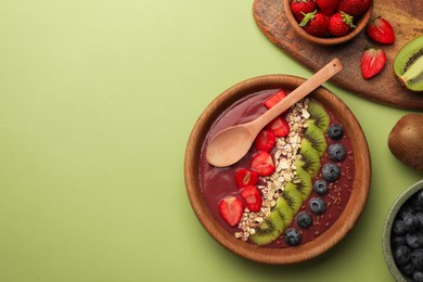 Photo of Bowl of delicious smoothie with fresh blueberries, strawberries, kiwi slices and oatmeal on light green background, flat lay. Space for text