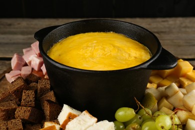 Photo of Fondue pot with melted cheese and different products on table, closeup