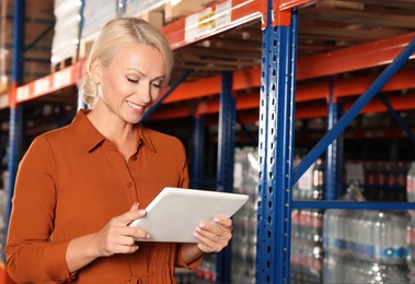Photo of Happy manager using modern tablet in warehouse with lots of products. Space for text