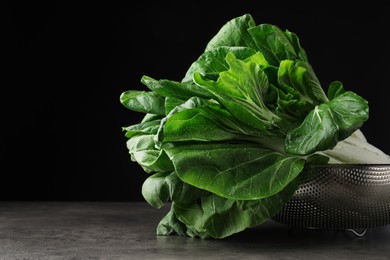 Photo of Fresh green pak choy cabbages with water drops in sieve on grey table. Space for text