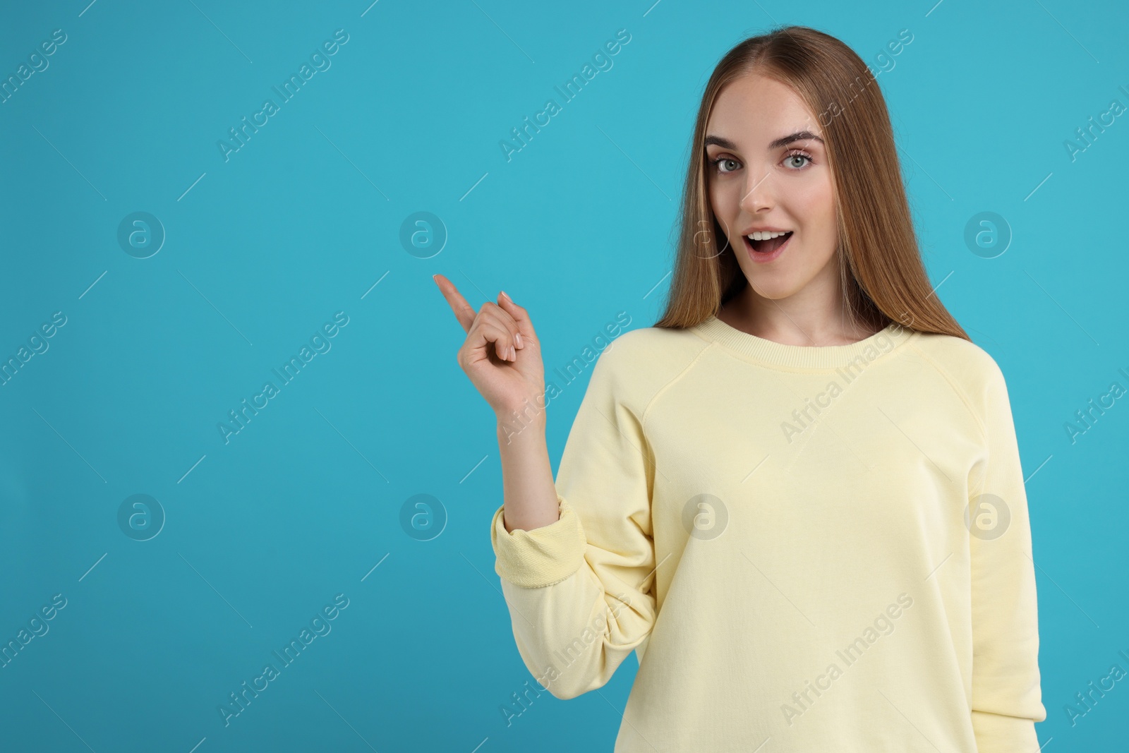 Photo of Special promotion. Emotional woman pointing at something on light blue background, space for text