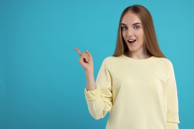 Photo of Special promotion. Emotional woman pointing at something on light blue background, space for text