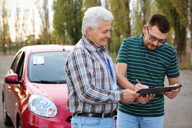 Photo of Senior instructor with clipboard and man outdoors. Get driving license