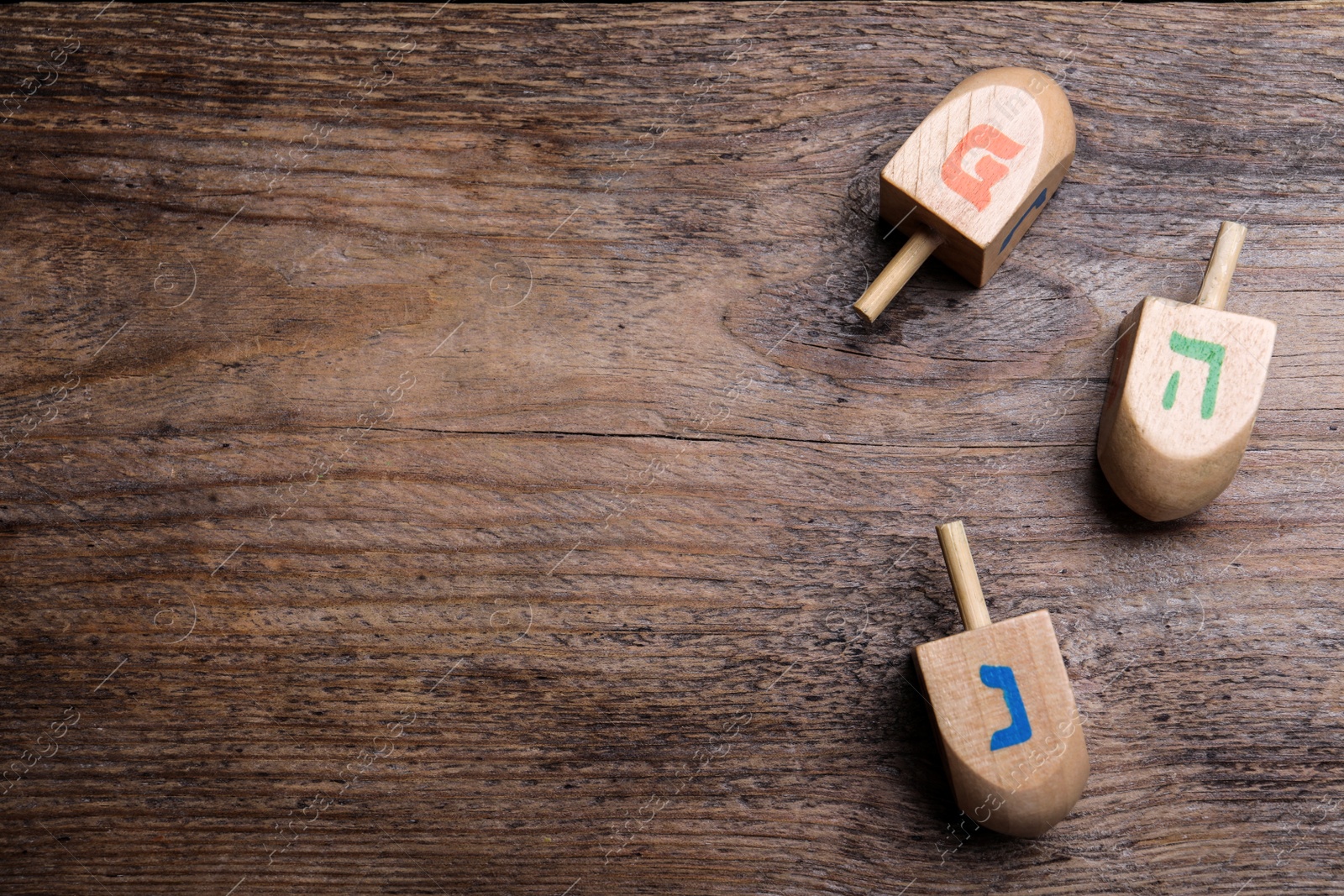 Photo of Hanukkah traditional dreidels with letters He, Pe and Nun on wooden table, flat lay. Space for text