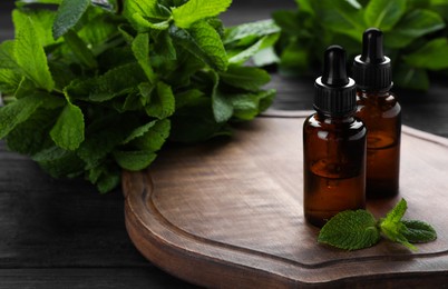 Photo of Bottles of mint essential oil and green leaves on black wooden table