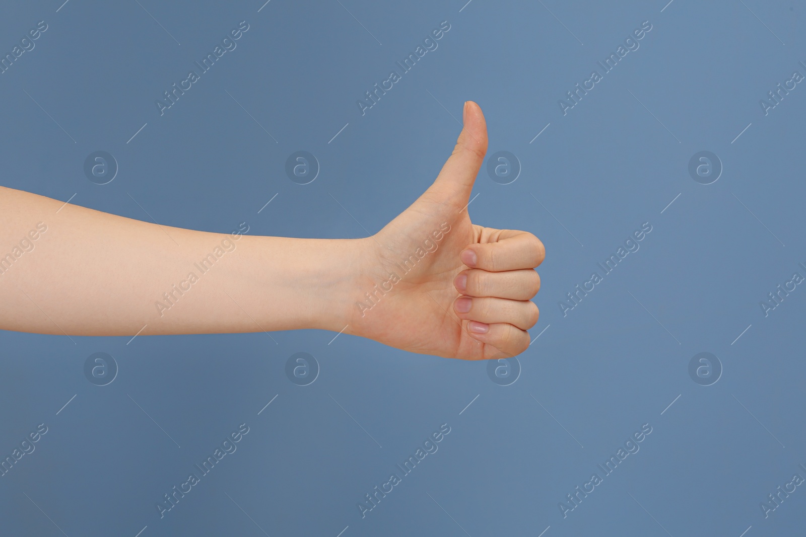 Photo of Woman showing thumb up on pale blue background, closeup