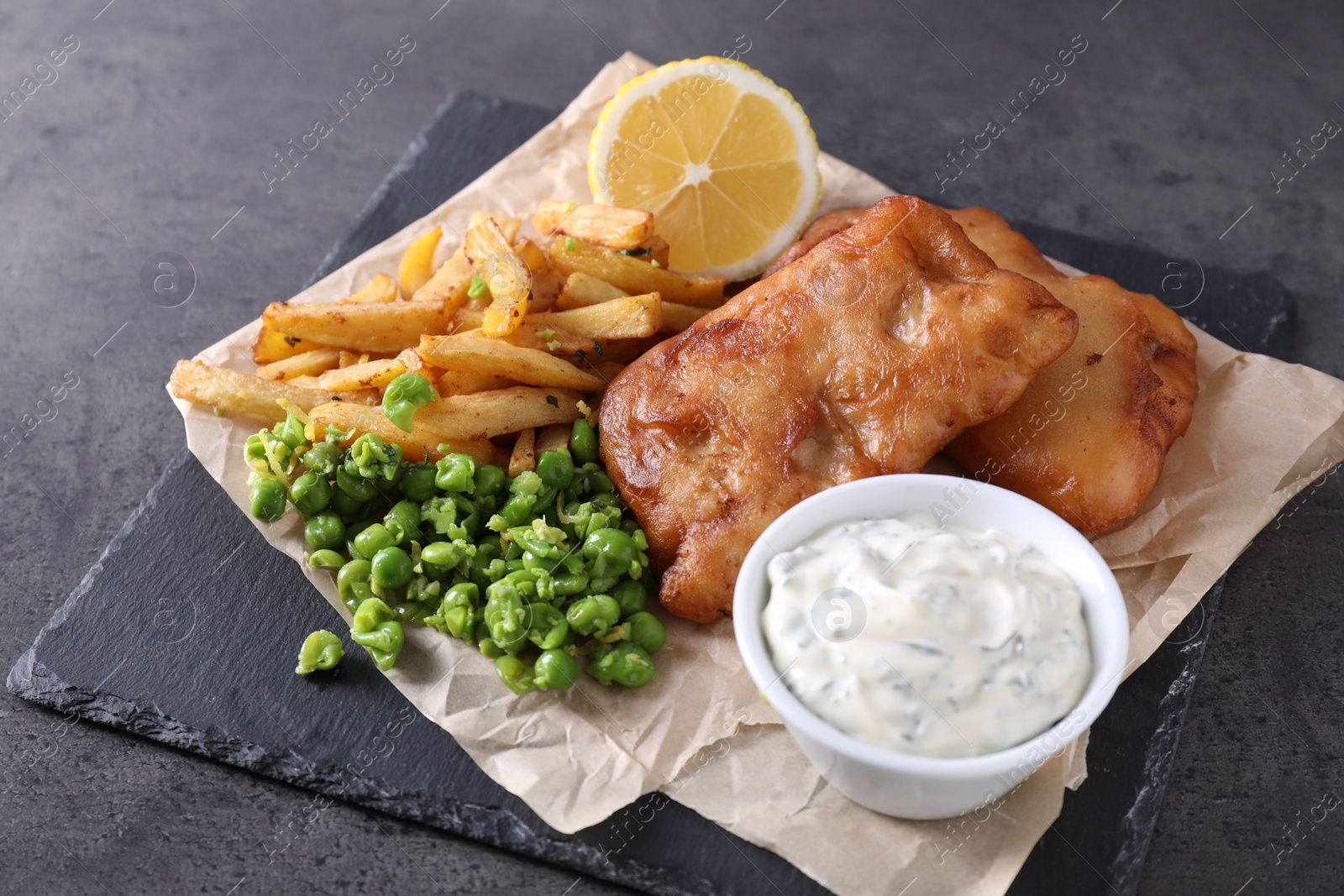 Photo of Tasty fish, chips, sauce and peas on grey table, closeup