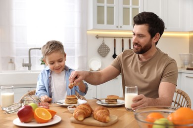 Father and his cute little son having breakfast at table in kitchen