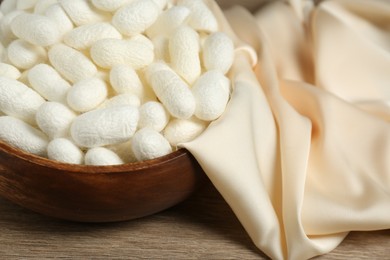 White cocoons with bowl and silk fabric on wooden table, closeup