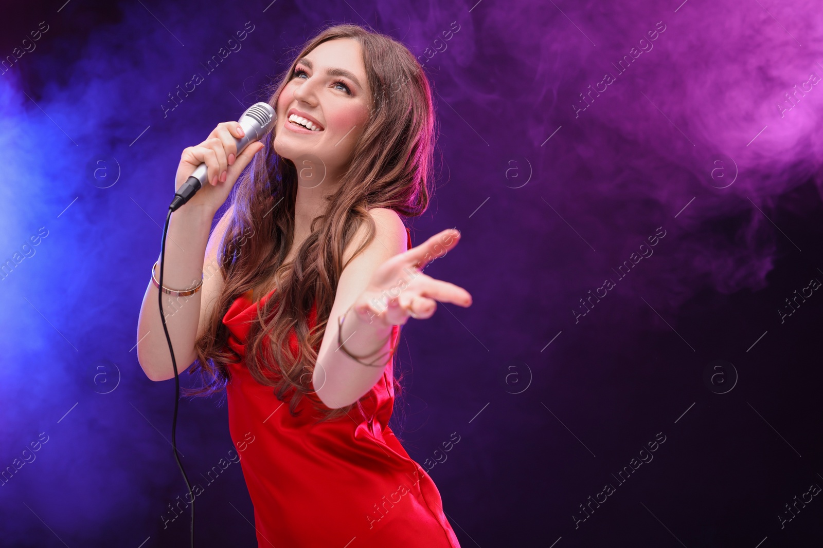 Photo of Emotional woman with microphone singing in color lights. Space for text