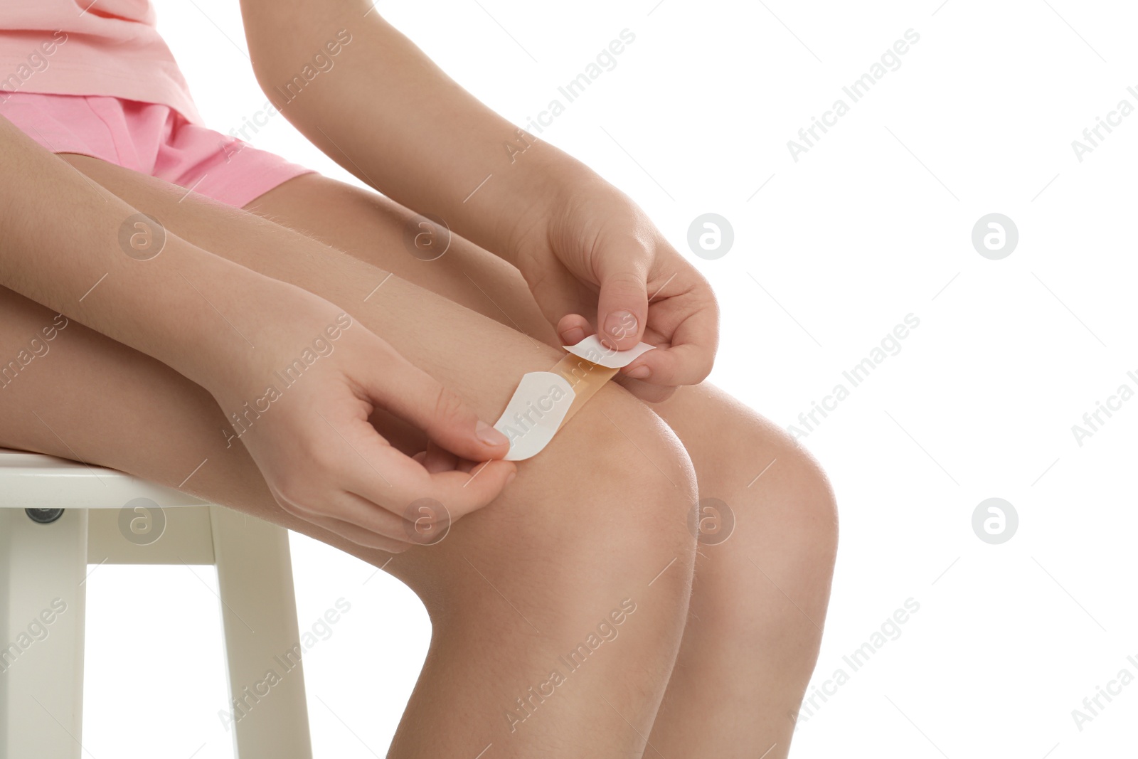 Photo of Girl putting sticking plaster onto leg on white background, closeup