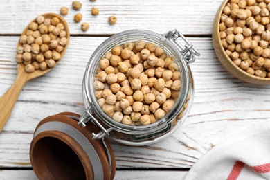 Photo of Raw chickpeas in jar on white wooden table, flat lay