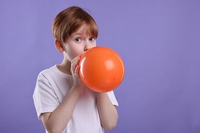 Photo of Boy inflating orange balloon on violet background, space for text
