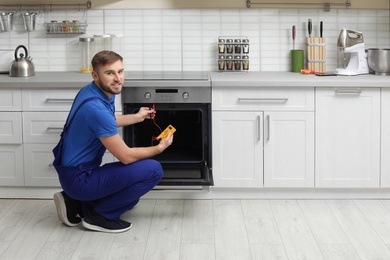 Photo of Professional serviceman repairing modern oven in kitchen