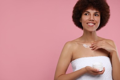 Beautiful young woman applying cream onto body on pink background, space for text