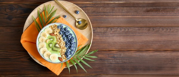 Image of Smoothie bowl with muesli, kiwi, banana, nuts and blueberries on wooden table, top view. Banner design with space for text