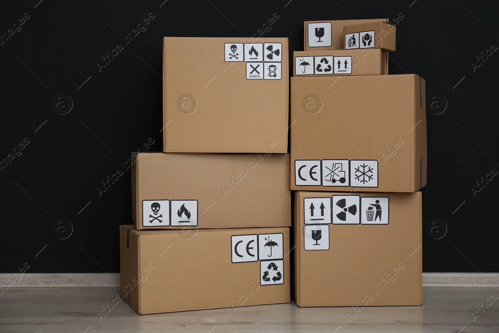 Photo of Cardboard boxes with different packaging symbols on floor near black wall. Parcel delivery