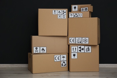 Photo of Cardboard boxes with different packaging symbols on floor near black wall. Parcel delivery