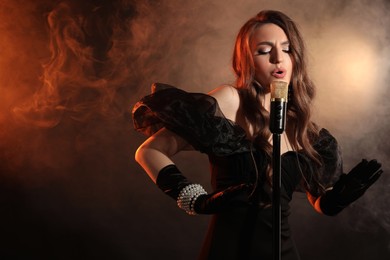 Beautiful young woman with microphone singing in color lights and smoke, space for text
