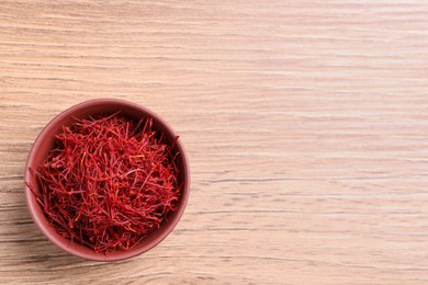 Dried saffron in bowl on wooden table, top view. Space for text