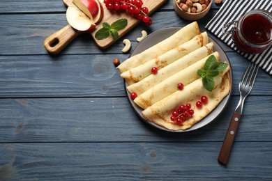 Photo of Delicious thin pancakes with berries on blue wooden table, flat lay. Space for text