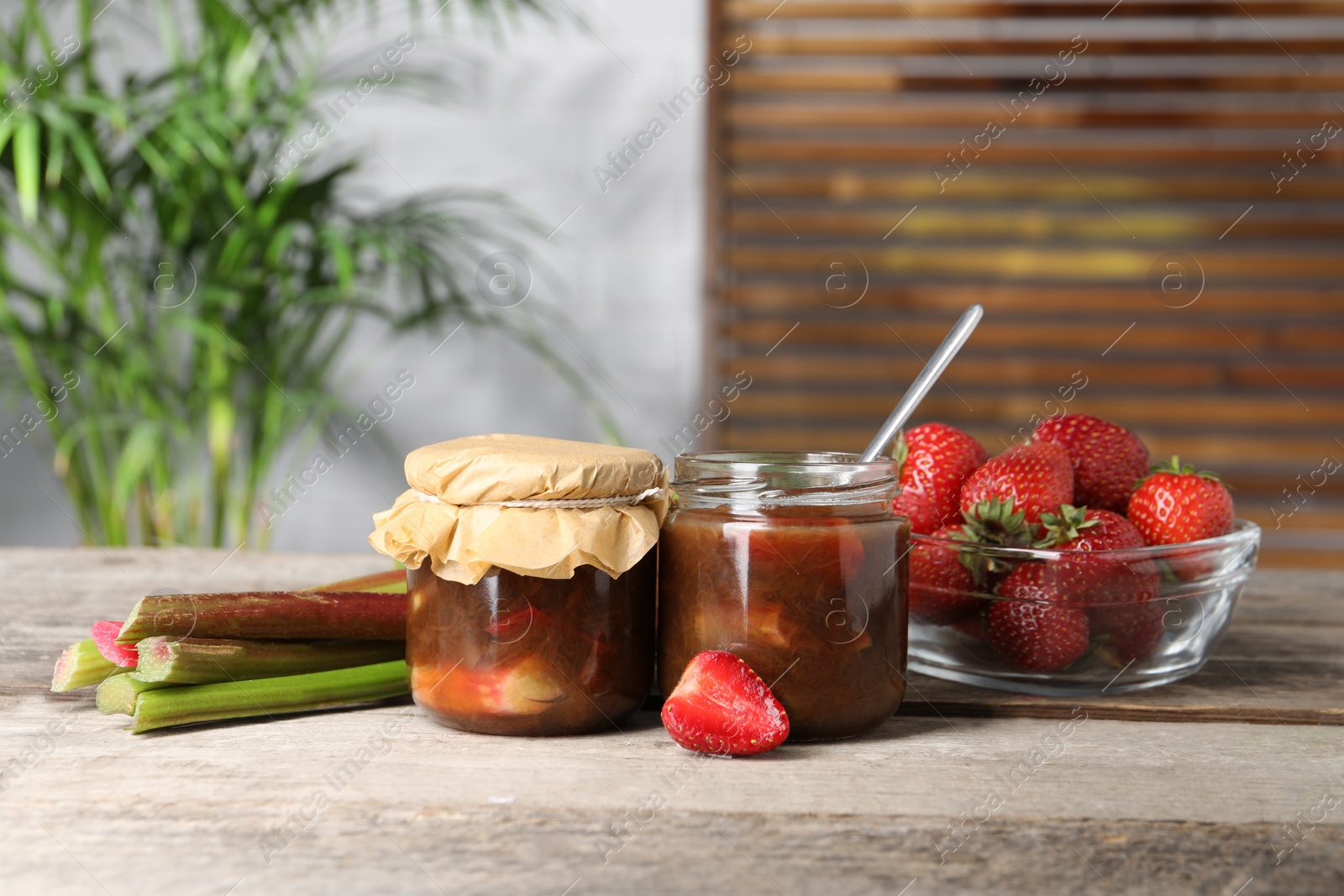 Photo of Jars of tasty rhubarb jam, fresh stems and strawberries on wooden table. Space for text