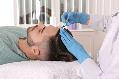 Photo of Young man with hair loss problem receiving injection in salon