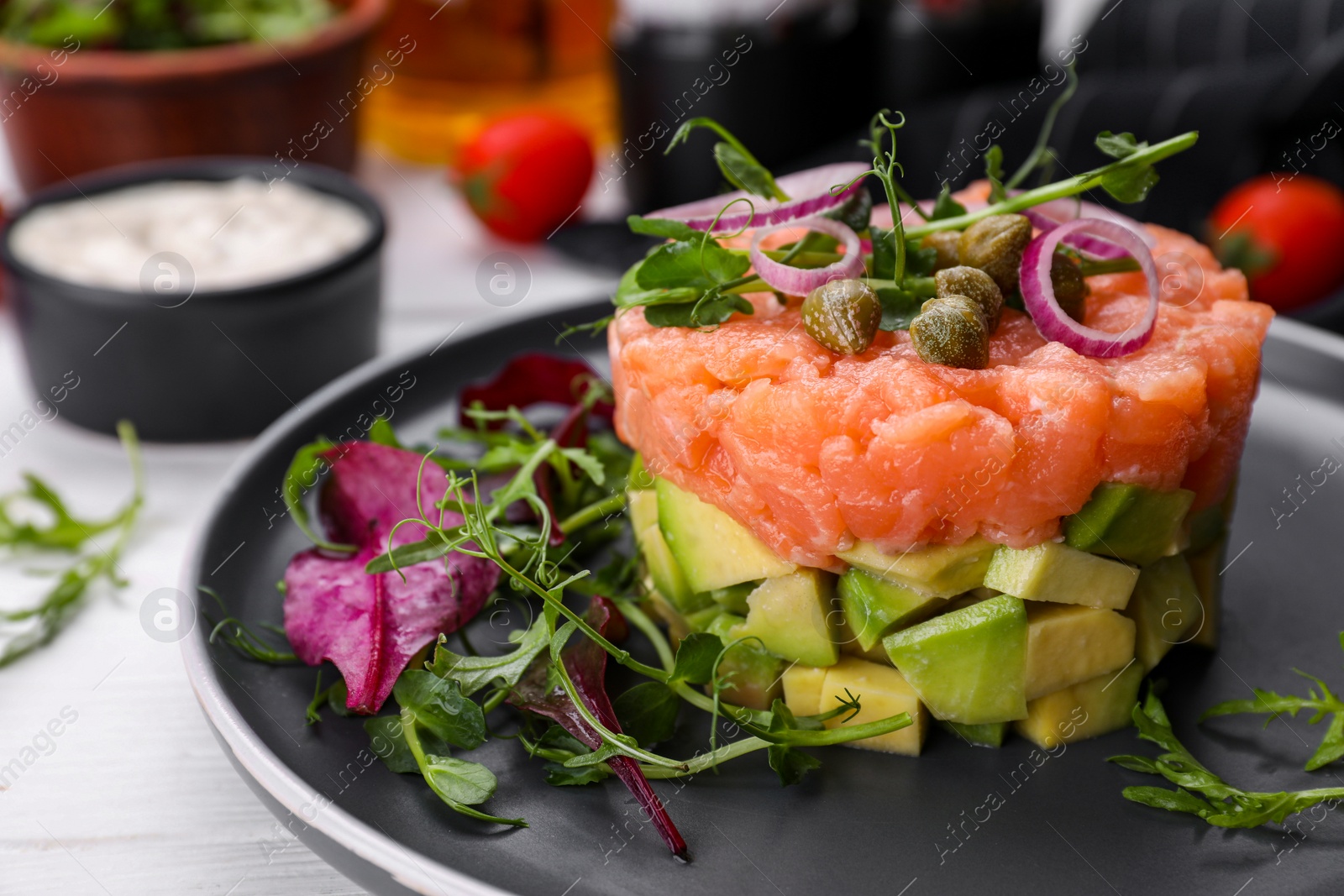 Photo of Tasty salmon tartare with avocado and greens on white table, closeup