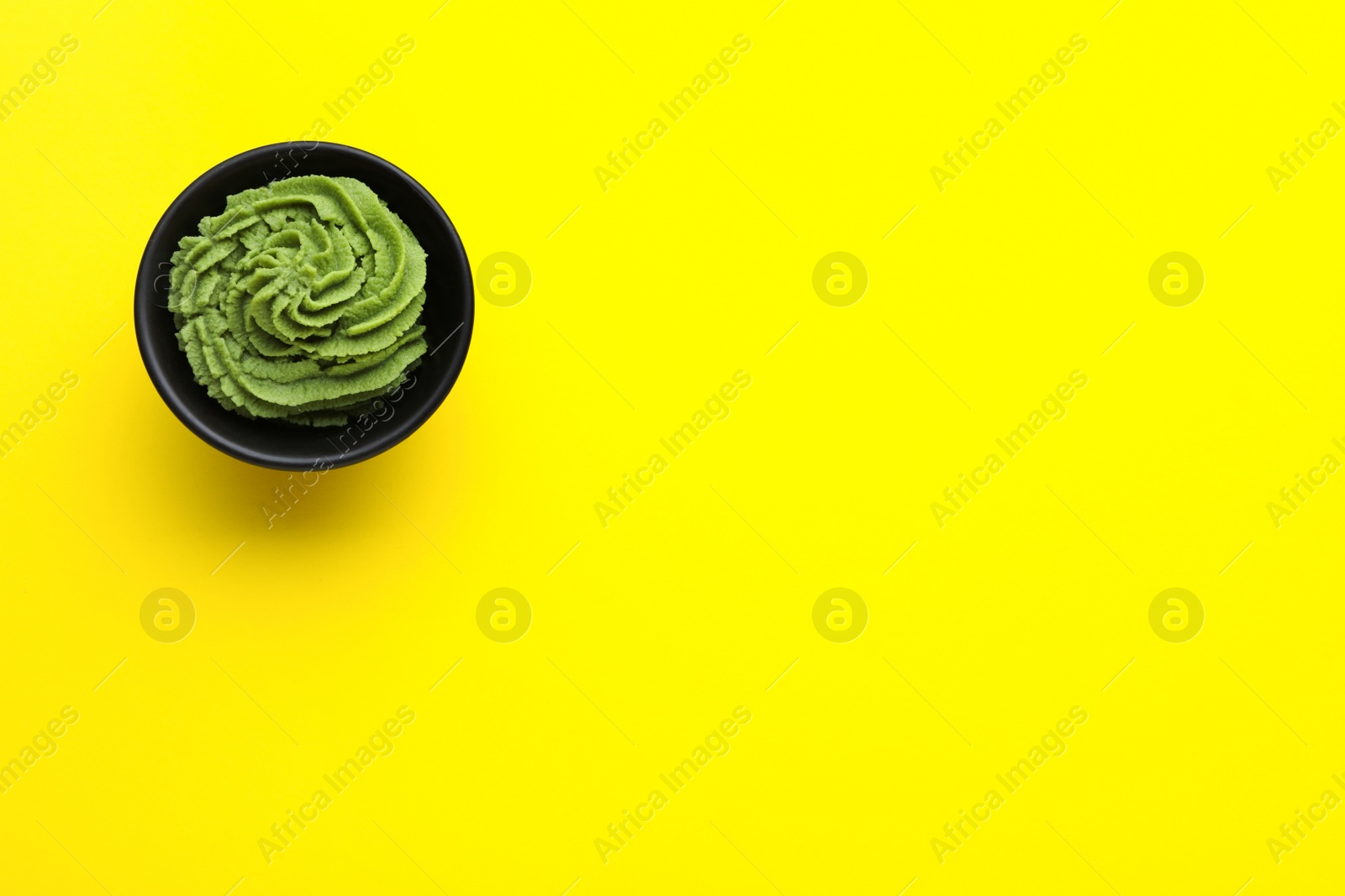 Photo of Bowl with swirl of wasabi paste on yellow background, top view. Space for text