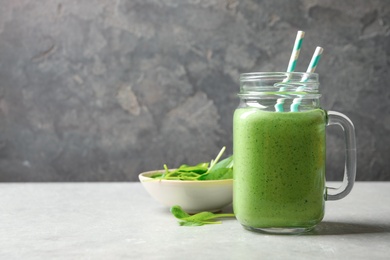 Photo of Mason jar of healthy green smoothie with fresh spinach on grey table, space for text