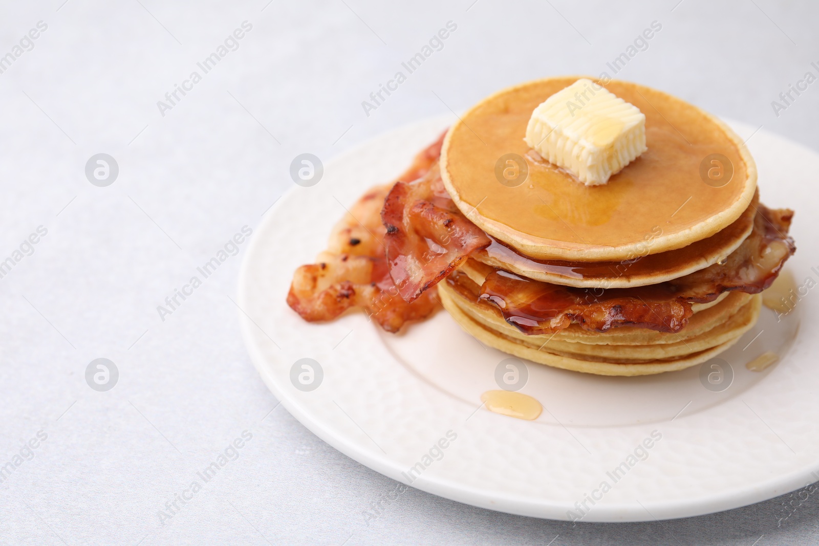 Photo of Delicious pancakes with bacon, butter and honey on light table, closeup. Space for text