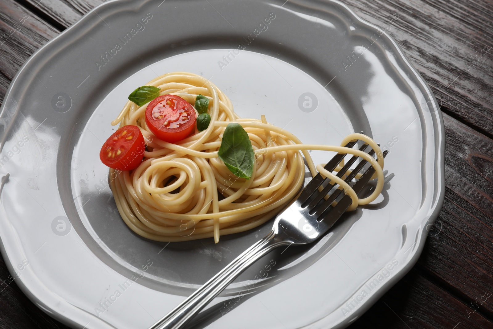 Photo of Heart made of tasty spaghetti, fork, tomato and basil on wooden table