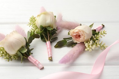Photo of Small stylish boutonnieres and ribbon on white wooden table