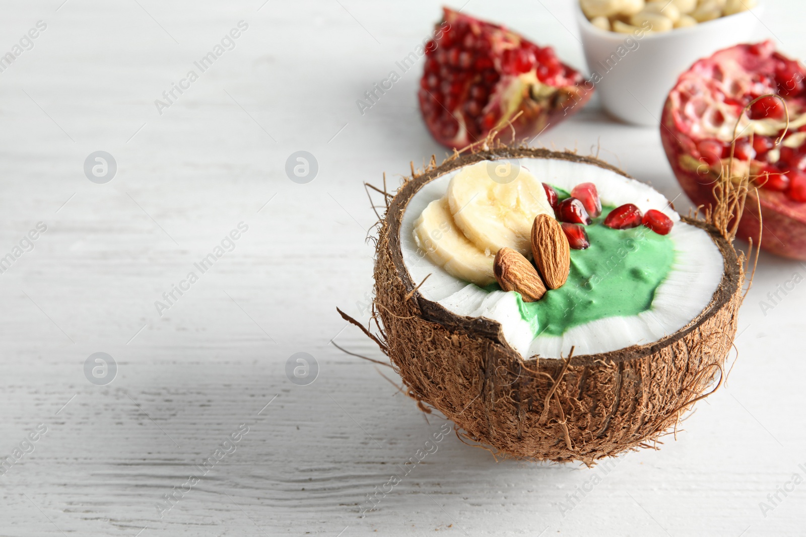 Photo of Yummy spirulina smoothie in coconut and pomegranate on wooden background. Space for text