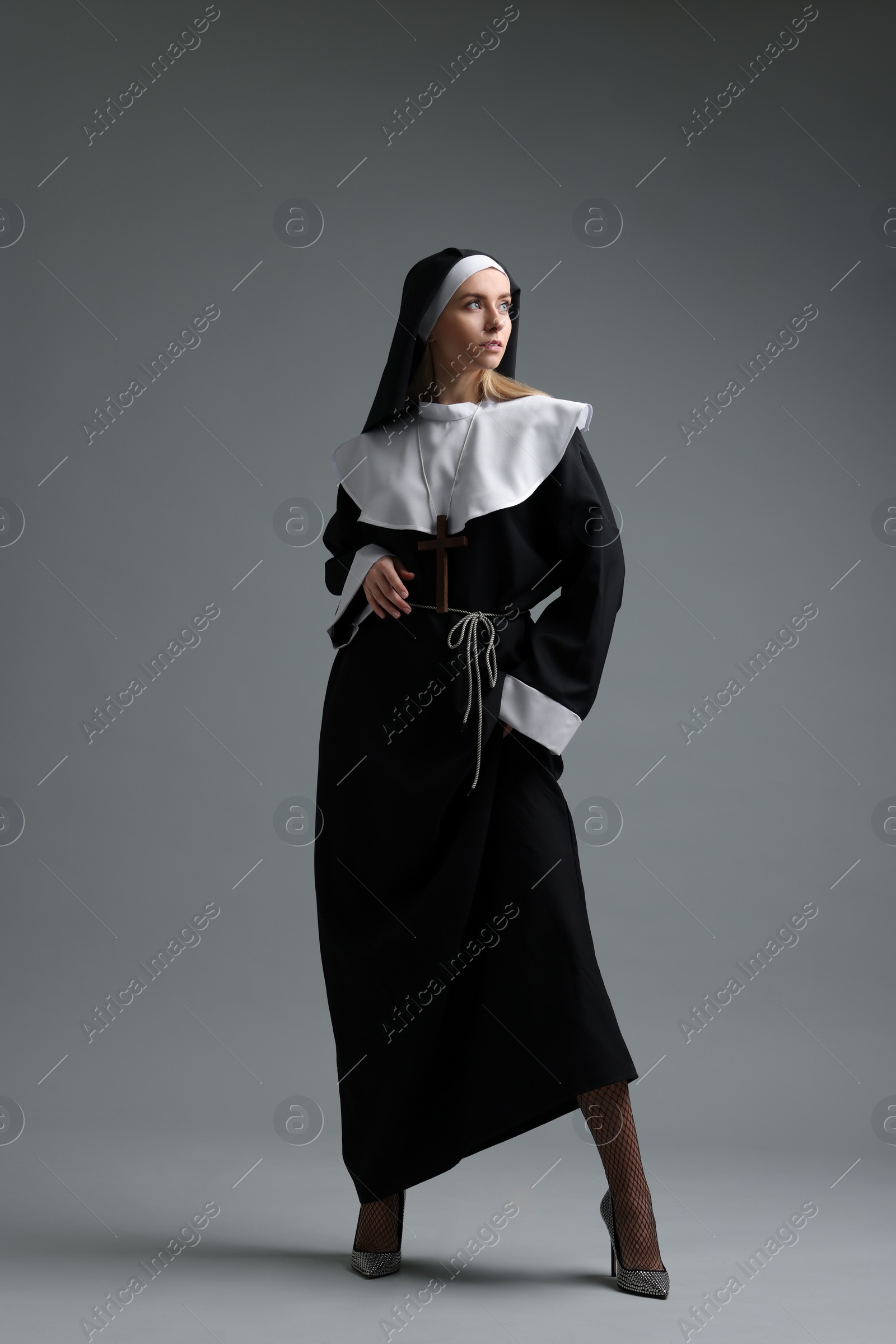 Photo of Woman in nun habit and mesh tights on grey background. Sexy costume