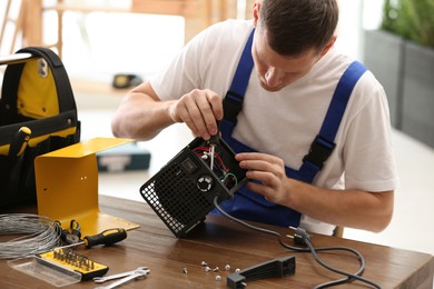 Photo of Professional technician repairing electric fan heater with screwdriver at table indoors